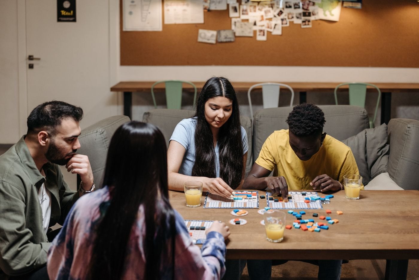 Four people gathered around tile boards at a wooden table