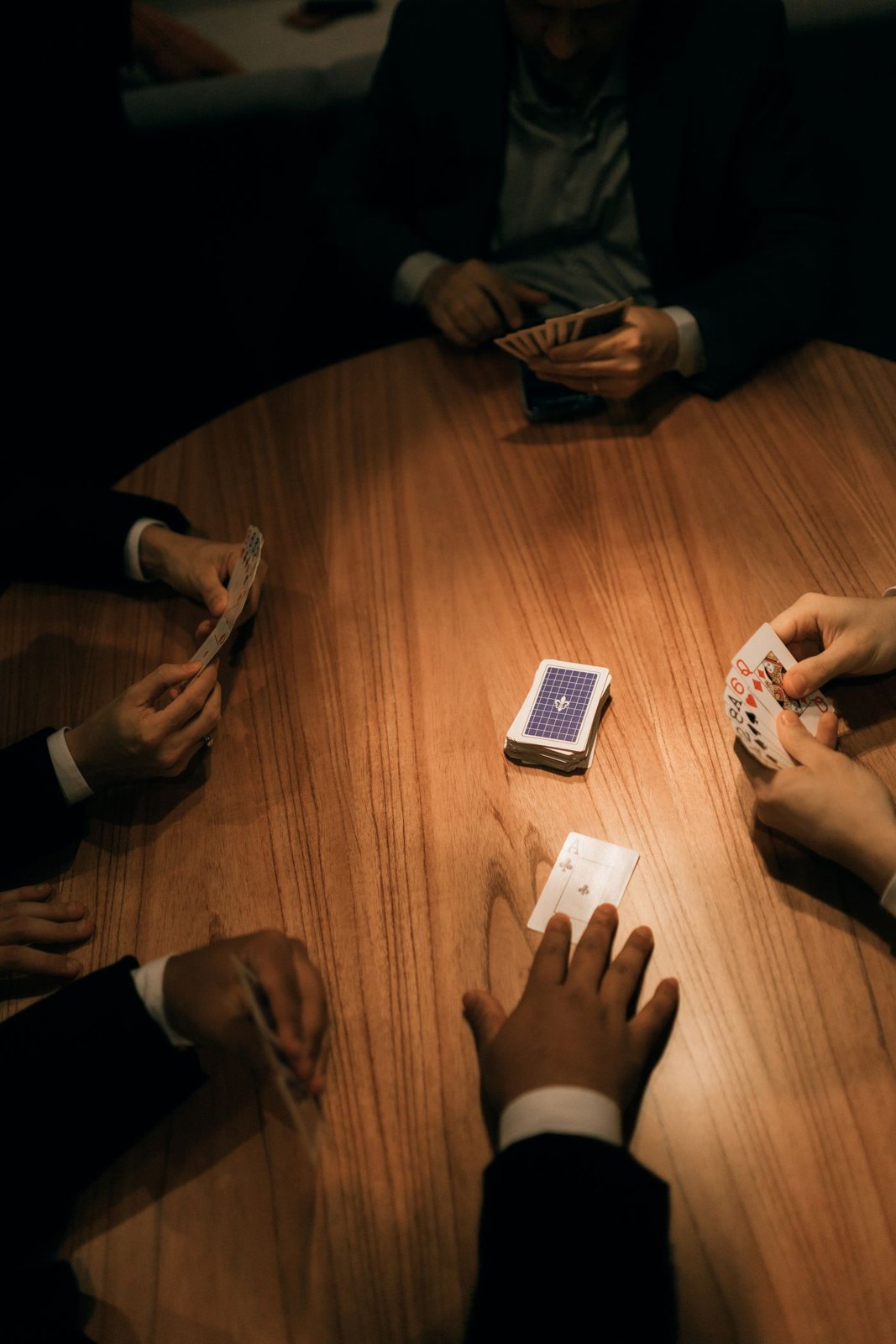 Players holding cards around a softly lit wooden table