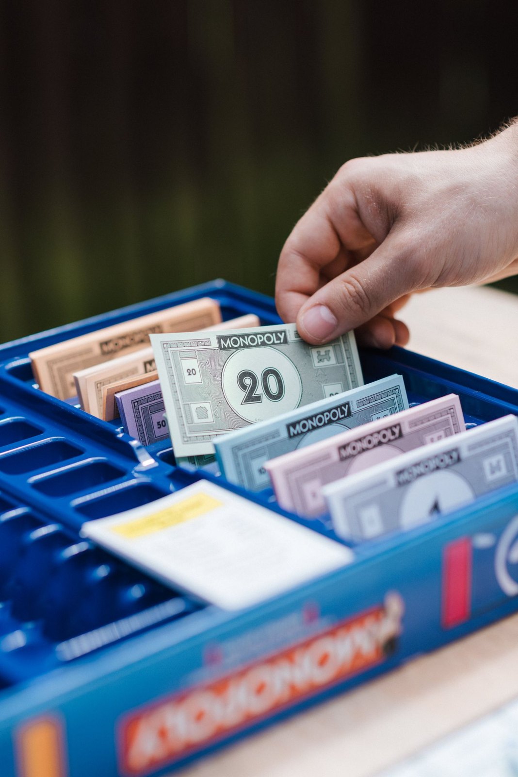 A hand selecting paper game money from a divided tray