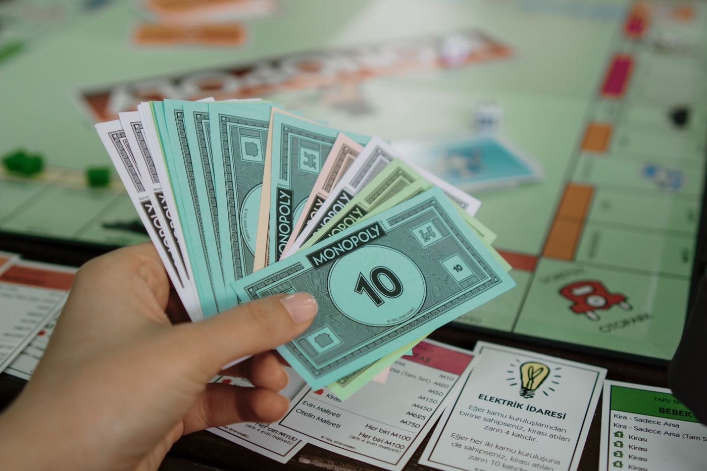 A hand holding paper game money above a board