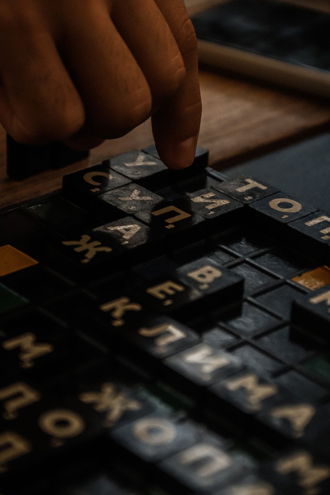 A hand selecting a wooden letter tile on a board